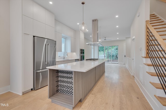 kitchen with white cabinets, a center island, light hardwood / wood-style flooring, appliances with stainless steel finishes, and island range hood