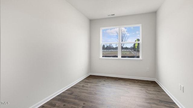 spare room featuring dark wood-type flooring, visible vents, and baseboards