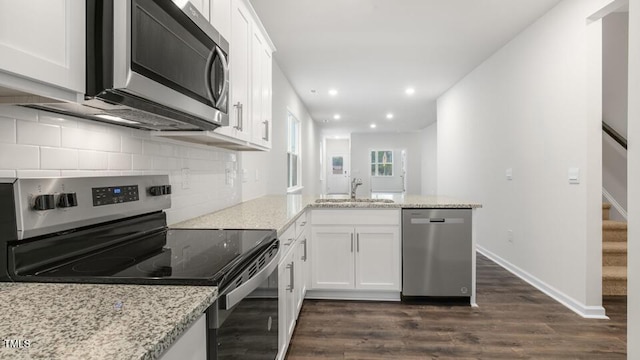 kitchen with tasteful backsplash, white cabinets, a peninsula, stainless steel appliances, and a sink