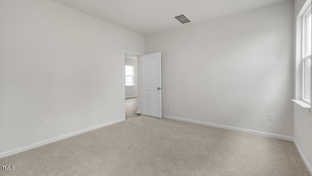 spare room with baseboards, visible vents, and light colored carpet