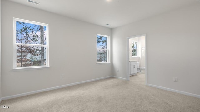 unfurnished bedroom featuring light carpet, visible vents, baseboards, and ensuite bathroom