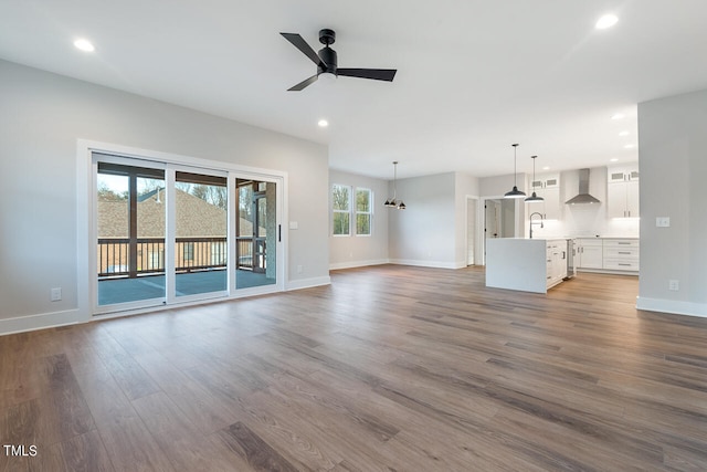 unfurnished living room with ceiling fan with notable chandelier, wood-type flooring, and a wealth of natural light