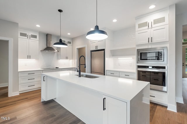 kitchen featuring stainless steel appliances, dark hardwood / wood-style flooring, an island with sink, wall chimney exhaust hood, and backsplash