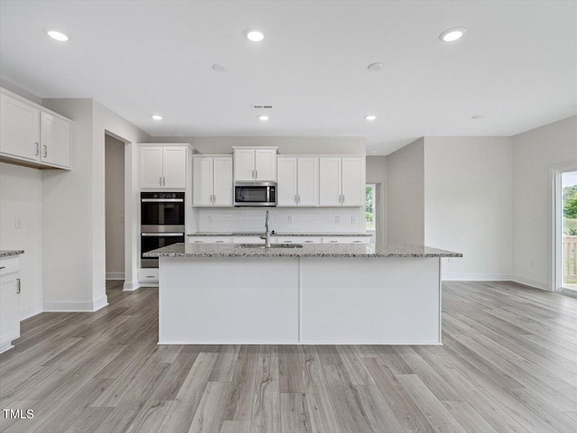 kitchen featuring a sink, white cabinetry, appliances with stainless steel finishes, backsplash, and an island with sink