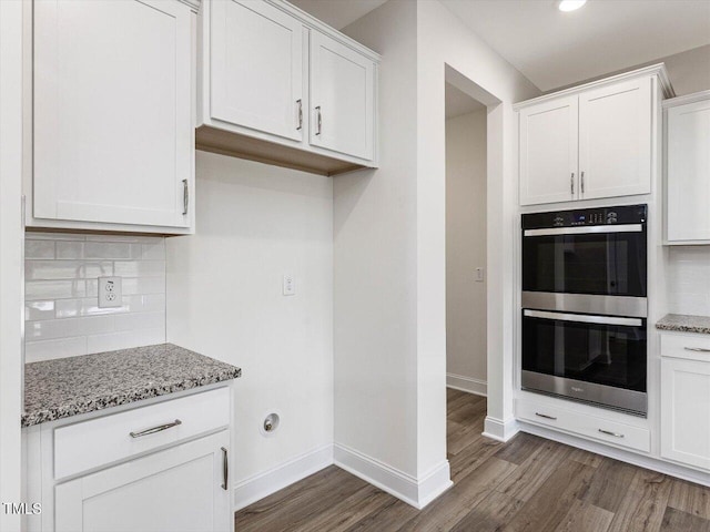 kitchen featuring light stone counters, dark wood finished floors, tasteful backsplash, double oven, and white cabinetry