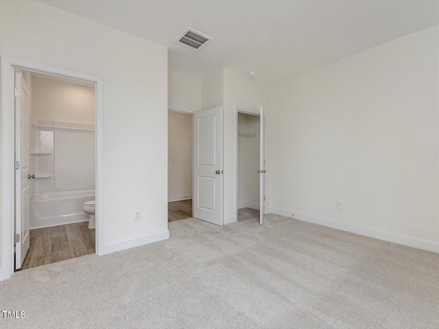 unfurnished bedroom featuring connected bathroom, carpet flooring, visible vents, and baseboards