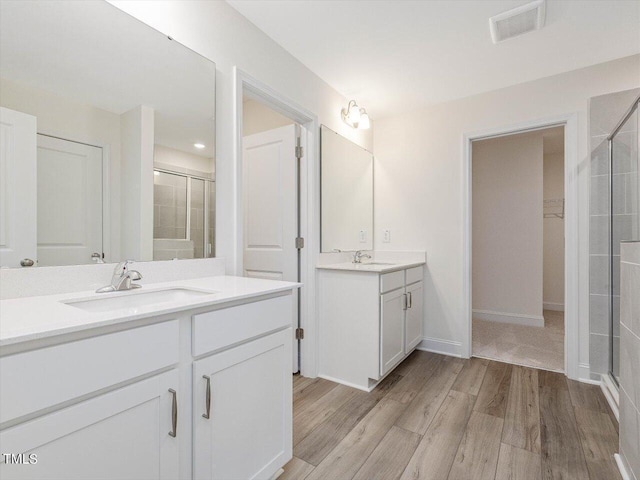 bathroom featuring visible vents, wood finished floors, a sink, a shower stall, and two vanities