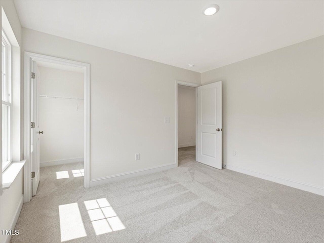 unfurnished bedroom featuring light carpet, a spacious closet, a closet, and baseboards