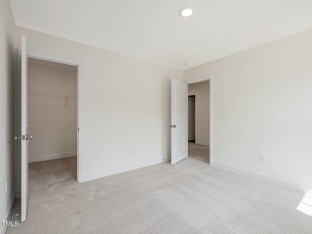 unfurnished bedroom with light carpet, baseboards, a walk in closet, and recessed lighting