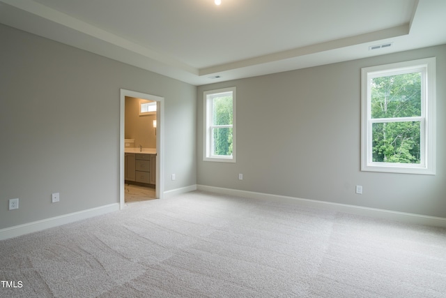 unfurnished bedroom featuring visible vents, baseboards, connected bathroom, light colored carpet, and a tray ceiling