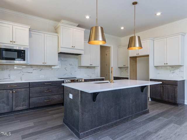 kitchen featuring a sink, stainless steel microwave, dark wood-style floors, and an island with sink
