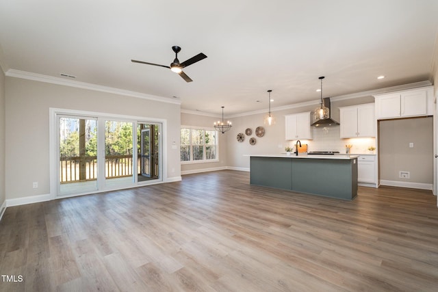kitchen featuring white cabinetry, a center island with sink, hanging light fixtures, and wall chimney range hood