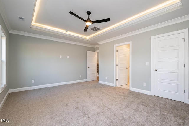 unfurnished bedroom with ceiling fan, light colored carpet, ornamental molding, and a tray ceiling