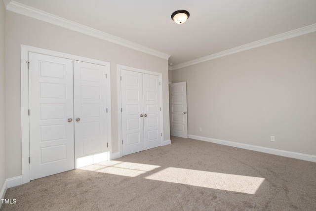 unfurnished bedroom with crown molding, light carpet, and two closets