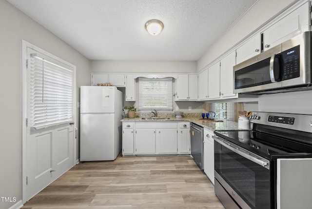 603 E Park St, Cary, NC 27511 - kitchen with stainless steel appliances, white cabinetry, light stone counters, light wood-style flooring, and a textured ceiling