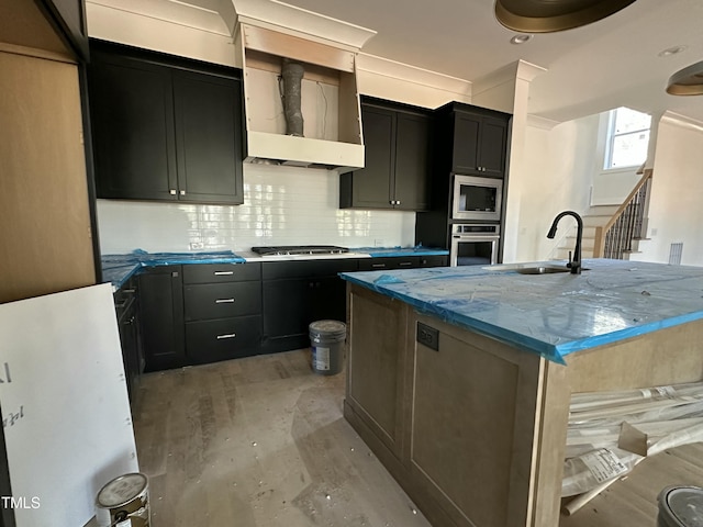 kitchen with sink, a center island with sink, stainless steel appliances, light stone countertops, and decorative backsplash