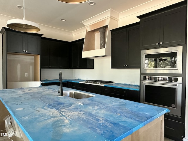 kitchen with stainless steel appliances, an island with sink, sink, and wall chimney range hood