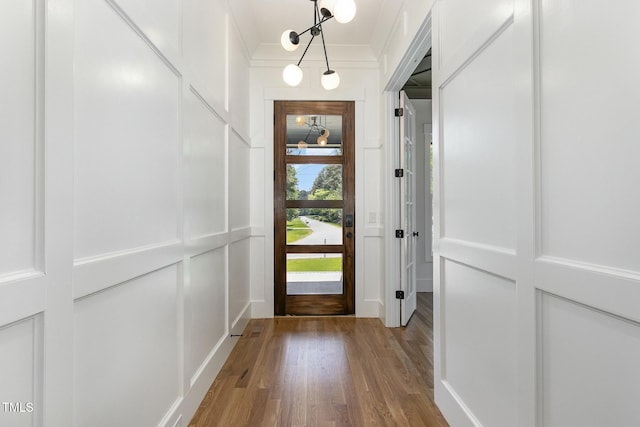 entryway featuring wood finished floors, an inviting chandelier, a decorative wall, and crown molding