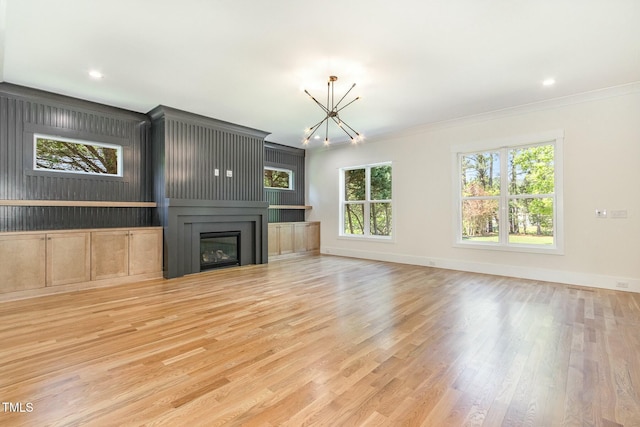unfurnished living room featuring a chandelier, wood finished floors, baseboards, and ornamental molding