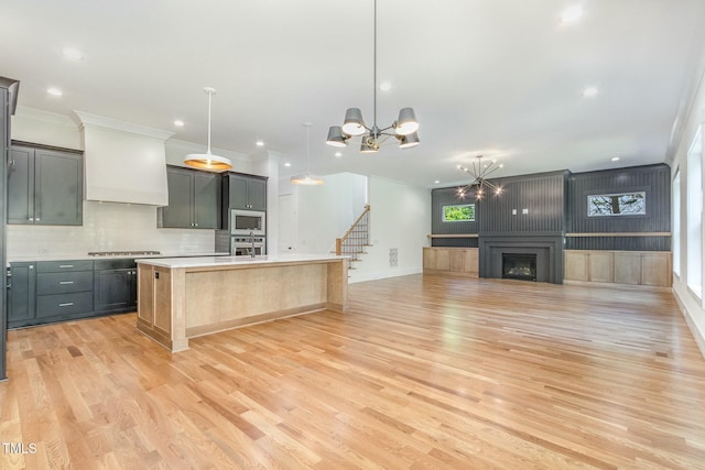 kitchen featuring an island with sink, light countertops, light wood-type flooring, tasteful backsplash, and appliances with stainless steel finishes