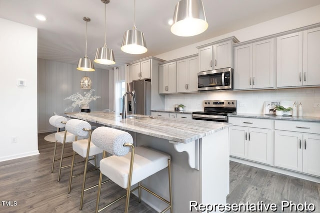 kitchen featuring hanging light fixtures, a center island with sink, a kitchen breakfast bar, and appliances with stainless steel finishes