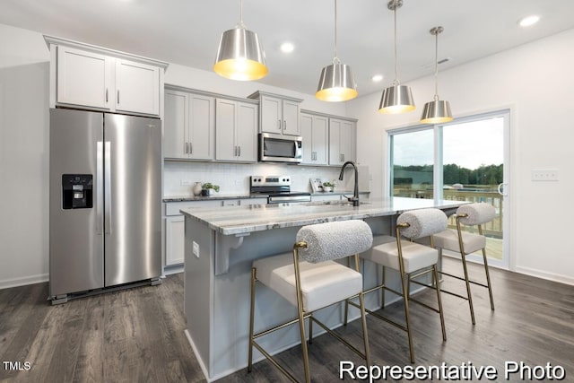 kitchen with pendant lighting, decorative backsplash, stainless steel appliances, and an island with sink