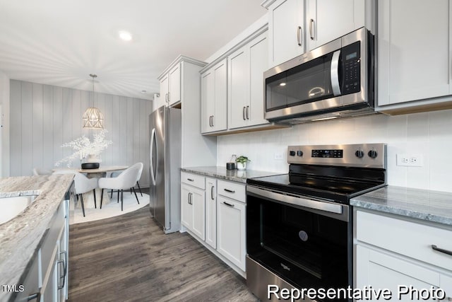 kitchen with appliances with stainless steel finishes, decorative light fixtures, white cabinets, dark hardwood / wood-style flooring, and light stone countertops