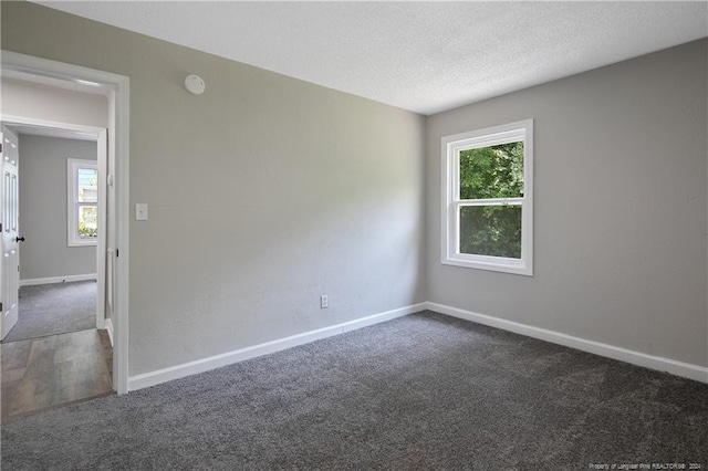 spare room featuring dark carpet and a textured ceiling