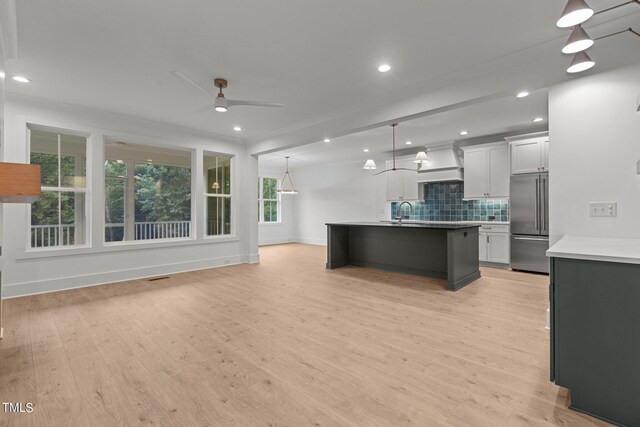 kitchen featuring white cabinets, pendant lighting, high quality fridge, light hardwood / wood-style flooring, and a center island with sink