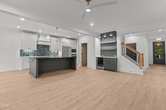 kitchen featuring light wood-style flooring, beverage cooler, a sink, white cabinets, and built in microwave