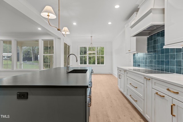 kitchen featuring custom range hood, hanging light fixtures, white cabinets, light hardwood / wood-style flooring, and sink