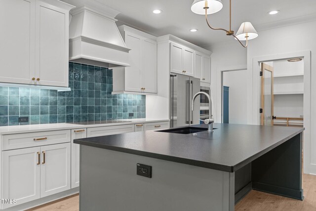 kitchen featuring premium range hood, white cabinets, pendant lighting, light hardwood / wood-style flooring, and a center island with sink