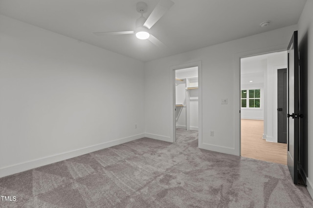 unfurnished bedroom featuring a closet, light colored carpet, ceiling fan, and a walk in closet