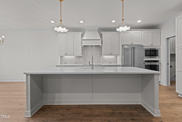 kitchen featuring a sink, appliances with stainless steel finishes, custom exhaust hood, decorative backsplash, and an island with sink