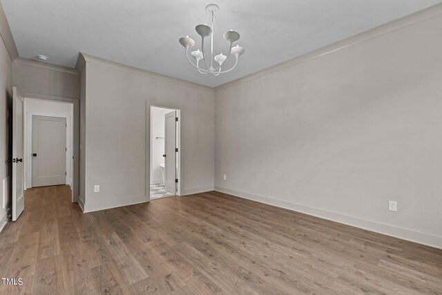 unfurnished bedroom featuring a notable chandelier, ensuite bath, baseboards, and wood finished floors