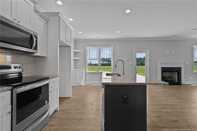 kitchen with a sink, white cabinets, appliances with stainless steel finishes, light stone countertops, and an island with sink