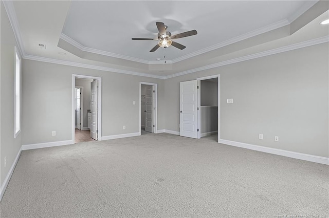 unfurnished bedroom featuring a tray ceiling, a walk in closet, light colored carpet, ornamental molding, and baseboards