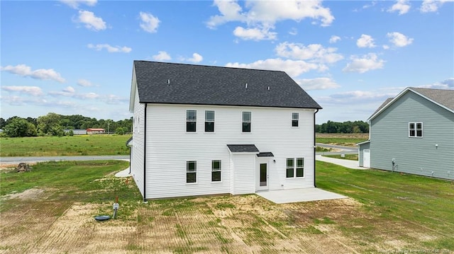 back of house with a shingled roof, a patio, and a lawn