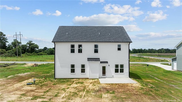 back of property with a yard, a shingled roof, and a patio