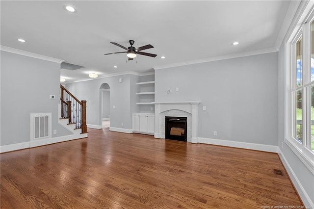 unfurnished living room featuring a brick fireplace, ceiling fan, crown molding, built in features, and hardwood / wood-style floors