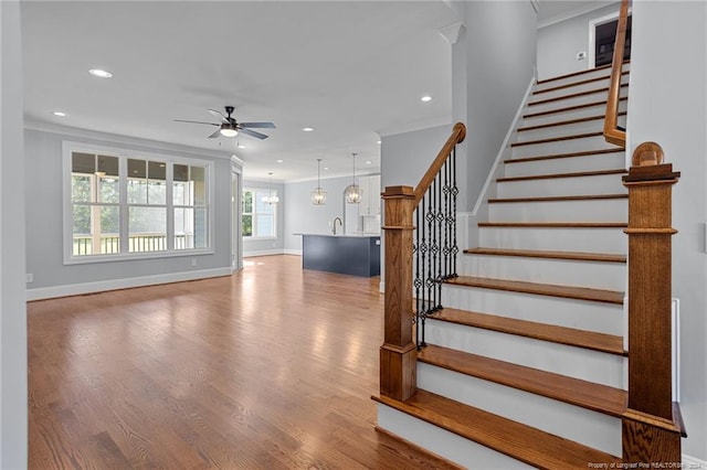 stairs featuring ceiling fan with notable chandelier, hardwood / wood-style flooring, and ornamental molding