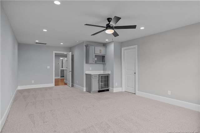 unfurnished living room with ceiling fan, light carpet, beverage cooler, and indoor bar