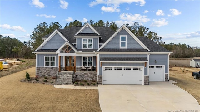 craftsman-style home featuring stone siding, french doors, board and batten siding, roof with shingles, and concrete driveway