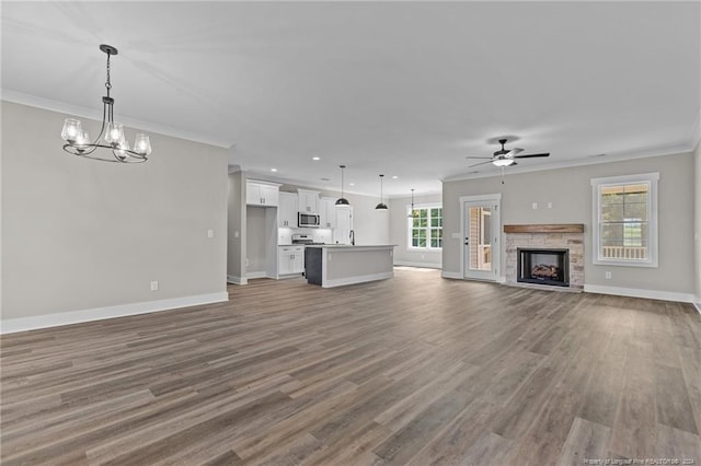 unfurnished living room with a fireplace, ceiling fan with notable chandelier, hardwood / wood-style floors, and ornamental molding