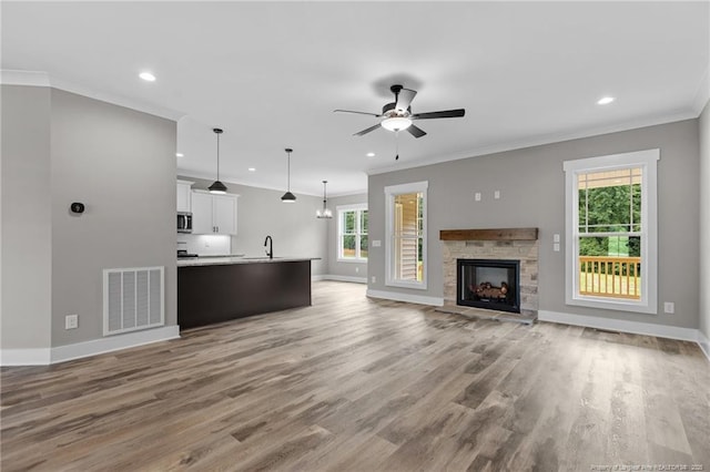 unfurnished living room with crown molding, a fireplace, visible vents, light wood-style flooring, and a sink