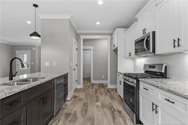 kitchen featuring light stone counters, decorative light fixtures, appliances with stainless steel finishes, white cabinets, and a sink