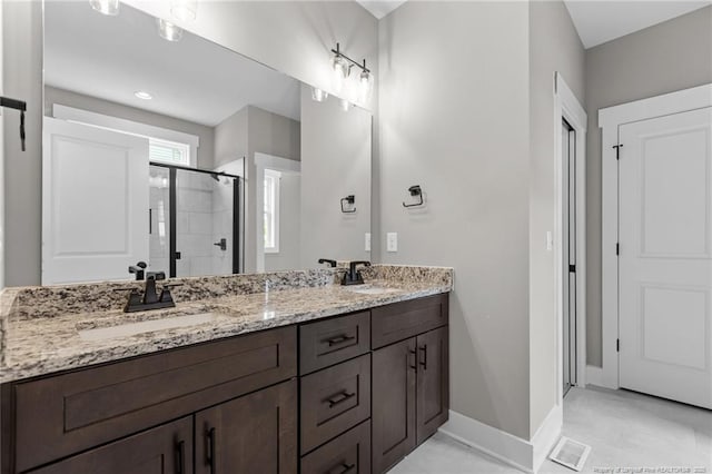 bathroom with double vanity, a shower stall, baseboards, and a sink