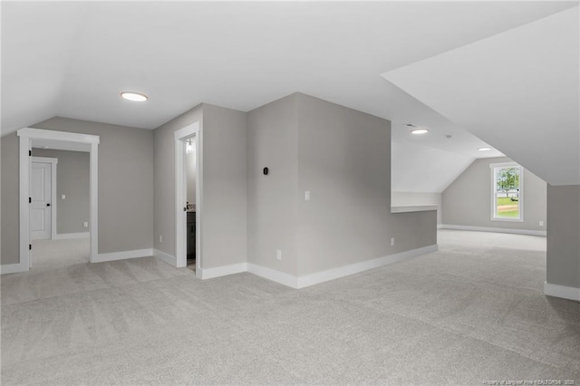 additional living space featuring baseboards, vaulted ceiling, and light colored carpet