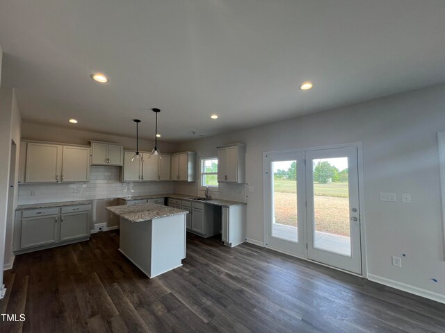 kitchen featuring dark hardwood / wood-style floors, decorative light fixtures, light stone countertops, backsplash, and a center island