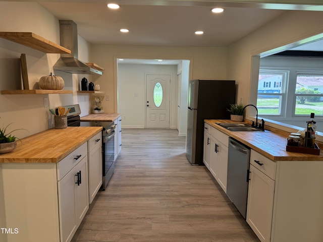 kitchen with wood counters, stainless steel appliances, white cabinets, and wall chimney range hood